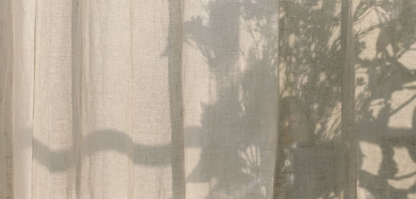 Heller Vorhang aus Leinen mit Schatten von Blättern im warmen Sonnenlicht
