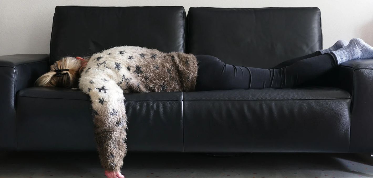 Emotionale Erschöpfung: Frau liegt kraftlos auf einem dunklen Sofa
